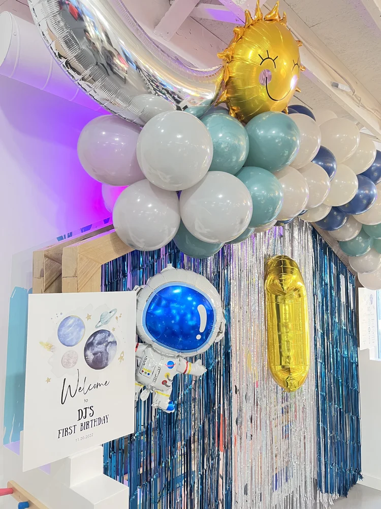 Space-themed first birthday at tumble HAUS with astronaut balloons, a smiling sun and silver fringe backdrop