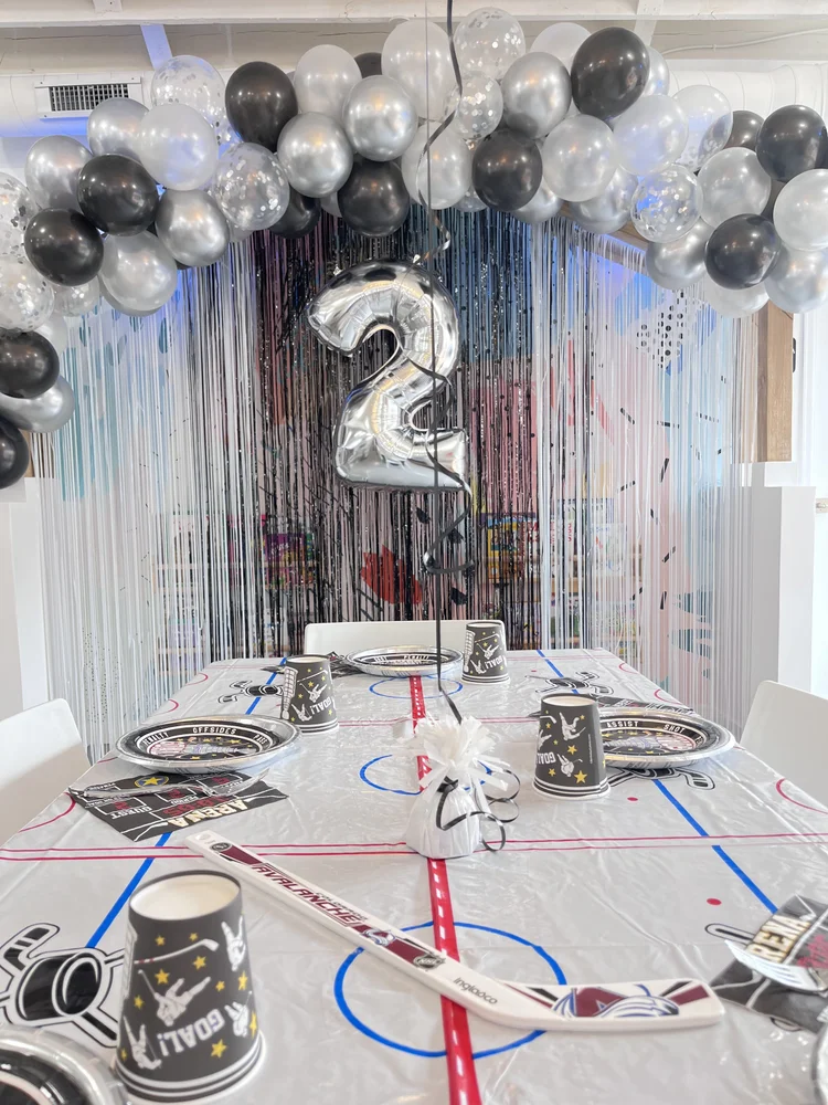 Hockey themed 2nd birthday party at tumble HAUS with silver and black balloon arch and an ice rink table cover