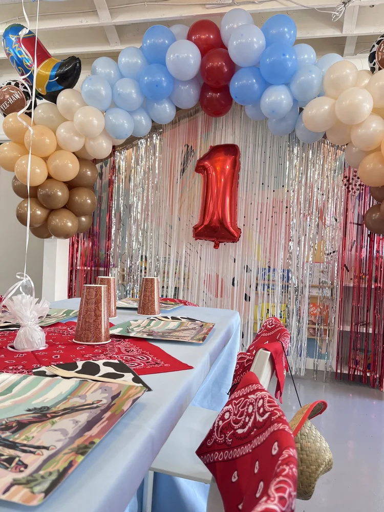Cowboy-themed first birthday party at tumble HAUS Denver with a blue, red and tan balloon arch and bandana table settings