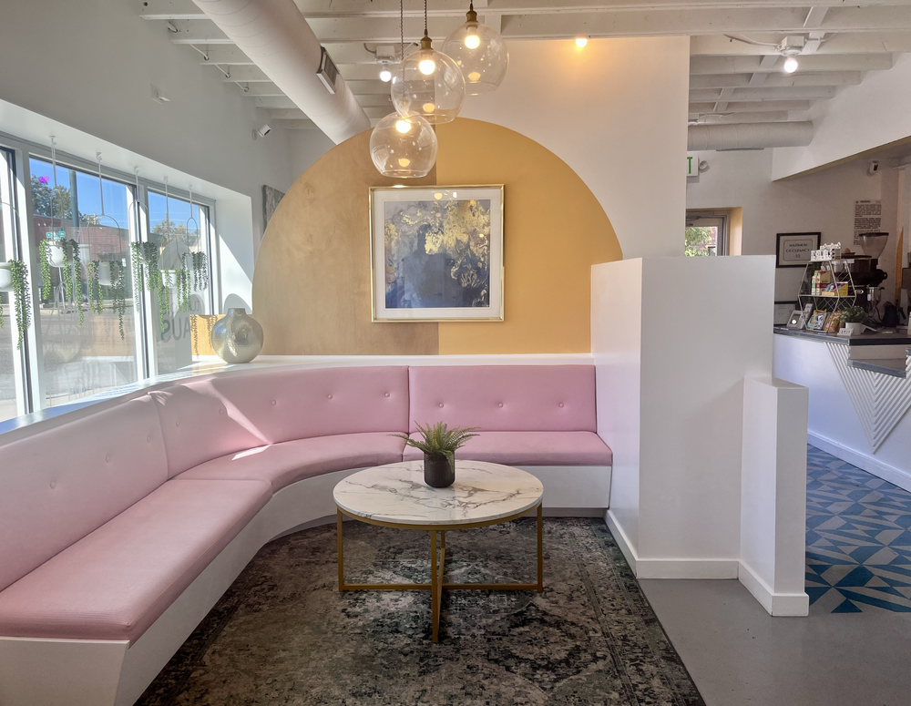 Cozy pink banquette lounge at tumble HAUS with a golden arch, framed art and a marble coffee table
