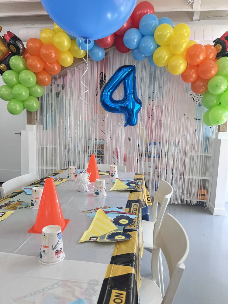 Construction truck themed 4th birthday party at tumble HAUS with rainbow balloon arch and traffic cone centerpieces