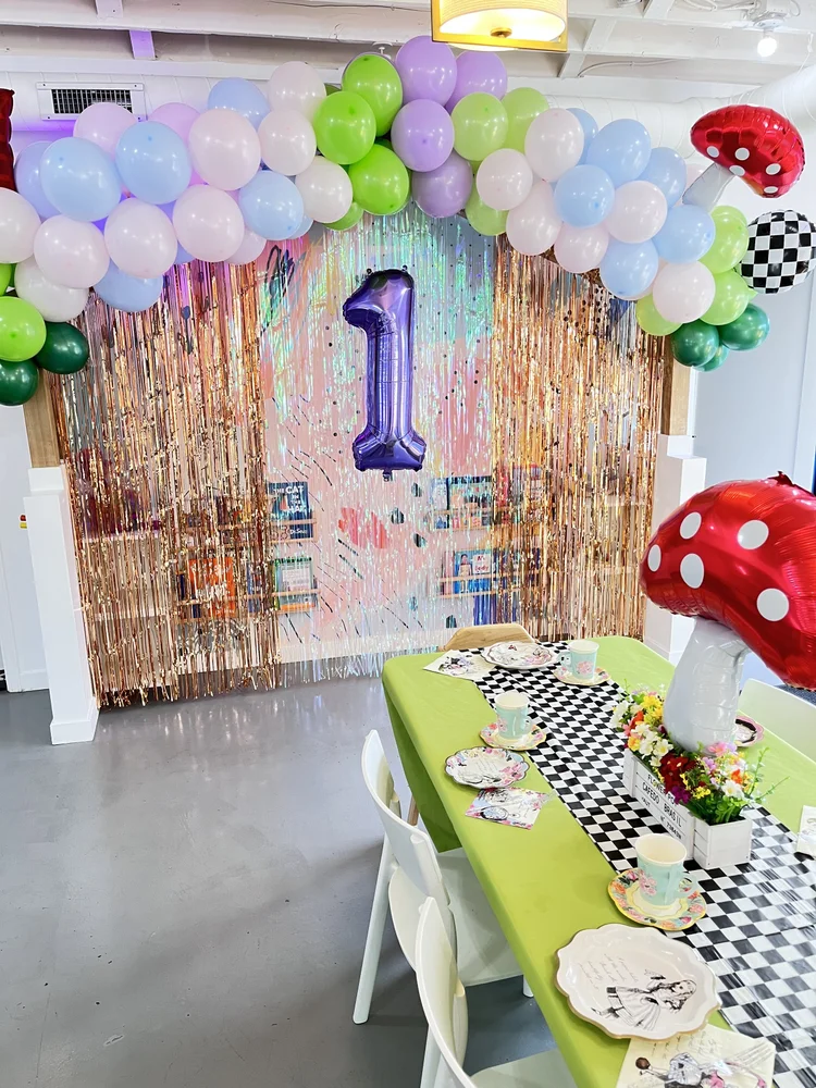 Pastel mushroom themed birthday party backdrop at tumble HAUS with a balloon arch and checkerboard table runner
