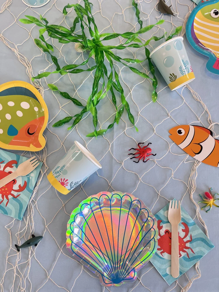 Under the sea birthday party table at tumble HAUS with shell plates, fish decor and a net table cover