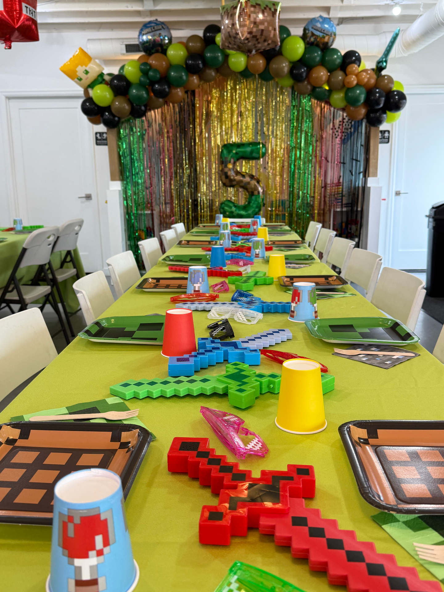 Minecraft themed 5th birthday party at tumble HAUS with a green and brown balloon arch, pixel swords and themed table settings