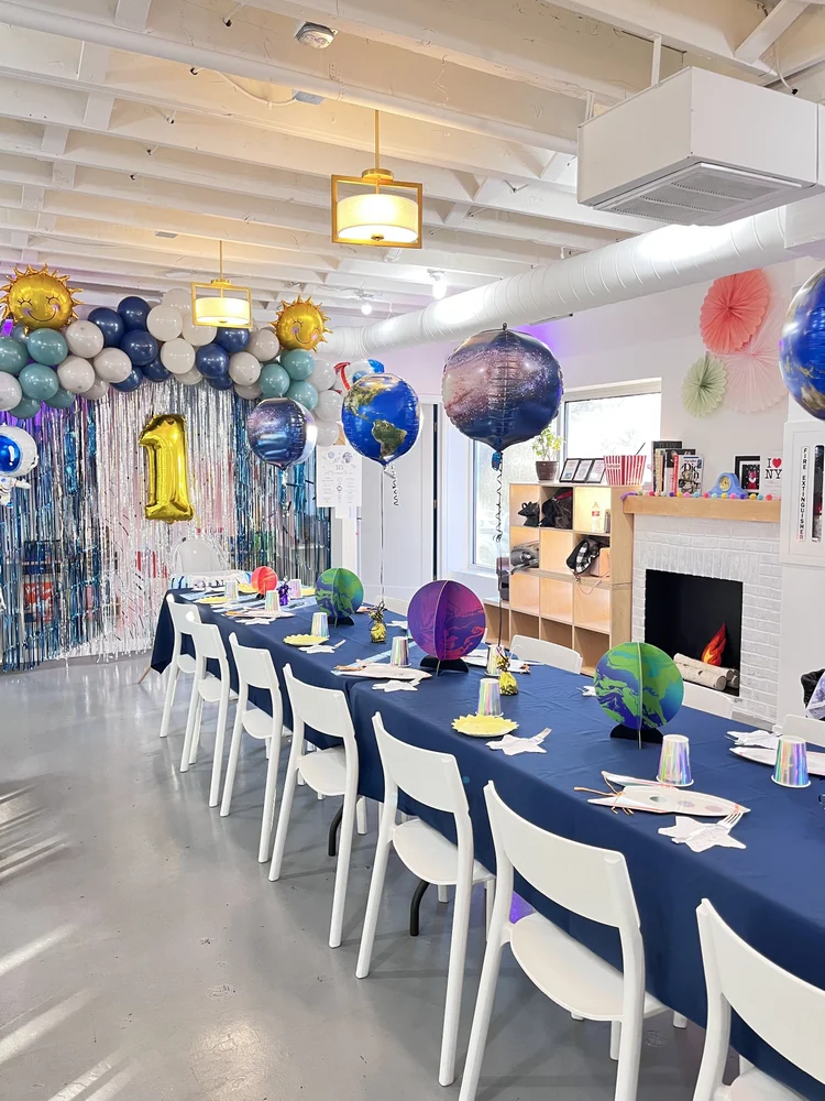 Outer space birthday party table at tumble HAUS with planet centerpieces, globe balloons and a navy table runner