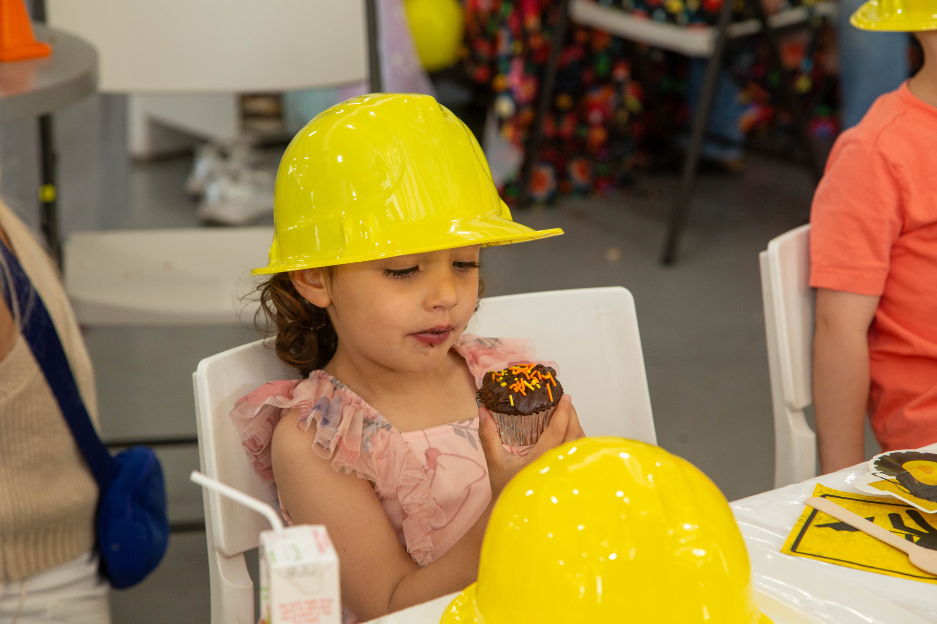 Young party guest in a yellow construction hat enjoying a chocolate cupcake