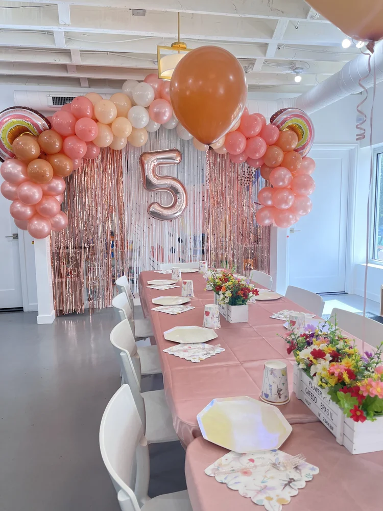 Peach and rose gold 5th birthday party at tumble HAUS with a balloon arch, fringe backdrop and floral centerpieces