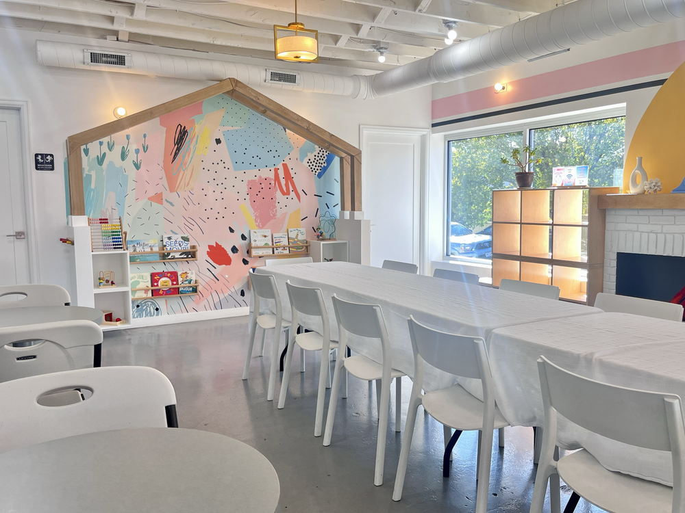 DIY party room at tumble HAUS with a colorful house mural, toy shelves and a long set table by the windows