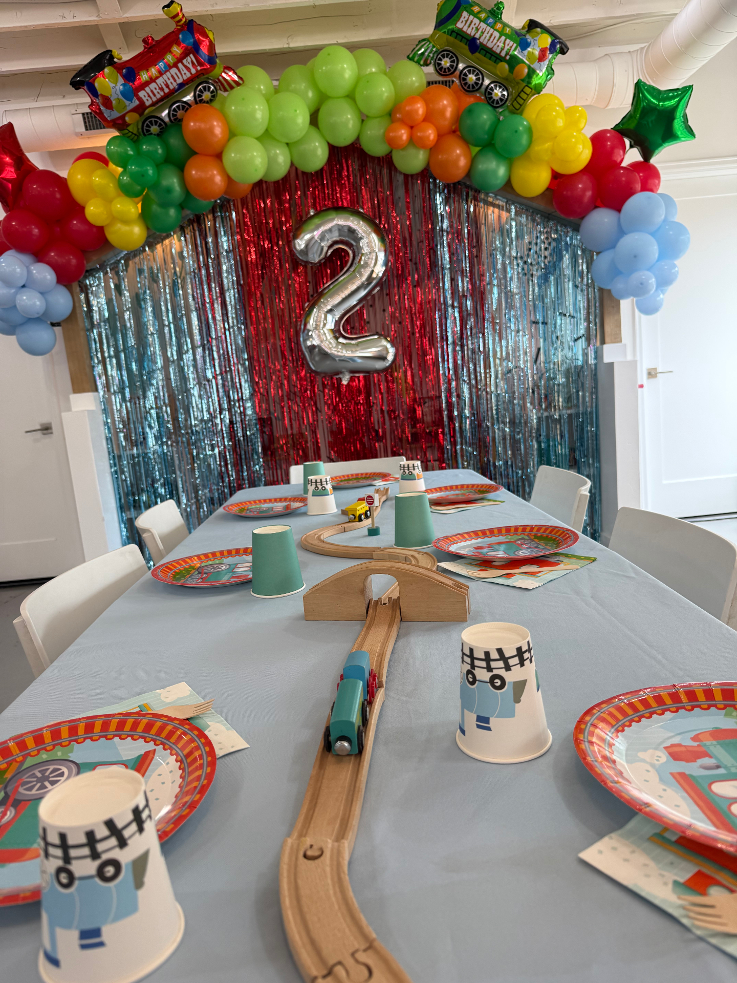 Train themed 2nd birthday party at tumble HAUS with a rainbow balloon arch, train balloons and a wooden train track centerpiece