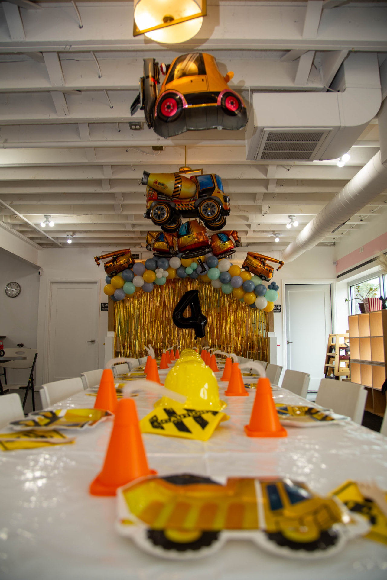 Construction-themed fourth birthday party at tumble HAUS with truck balloons, a yellow balloon arch, traffic cones and themed table settings