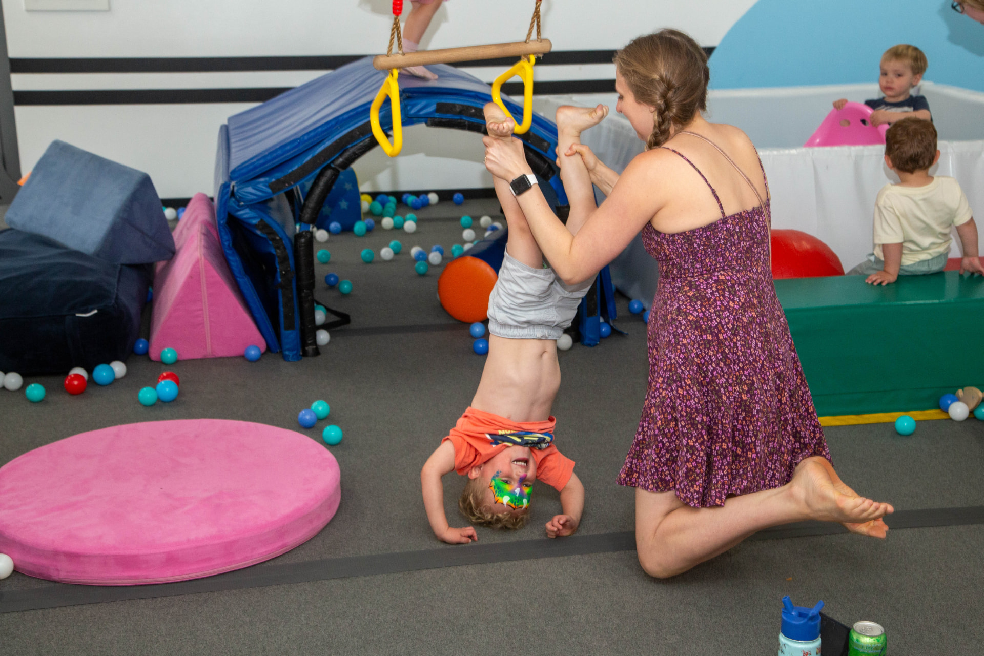 Caregiver helping a face-painted child tumble during an active birthday party