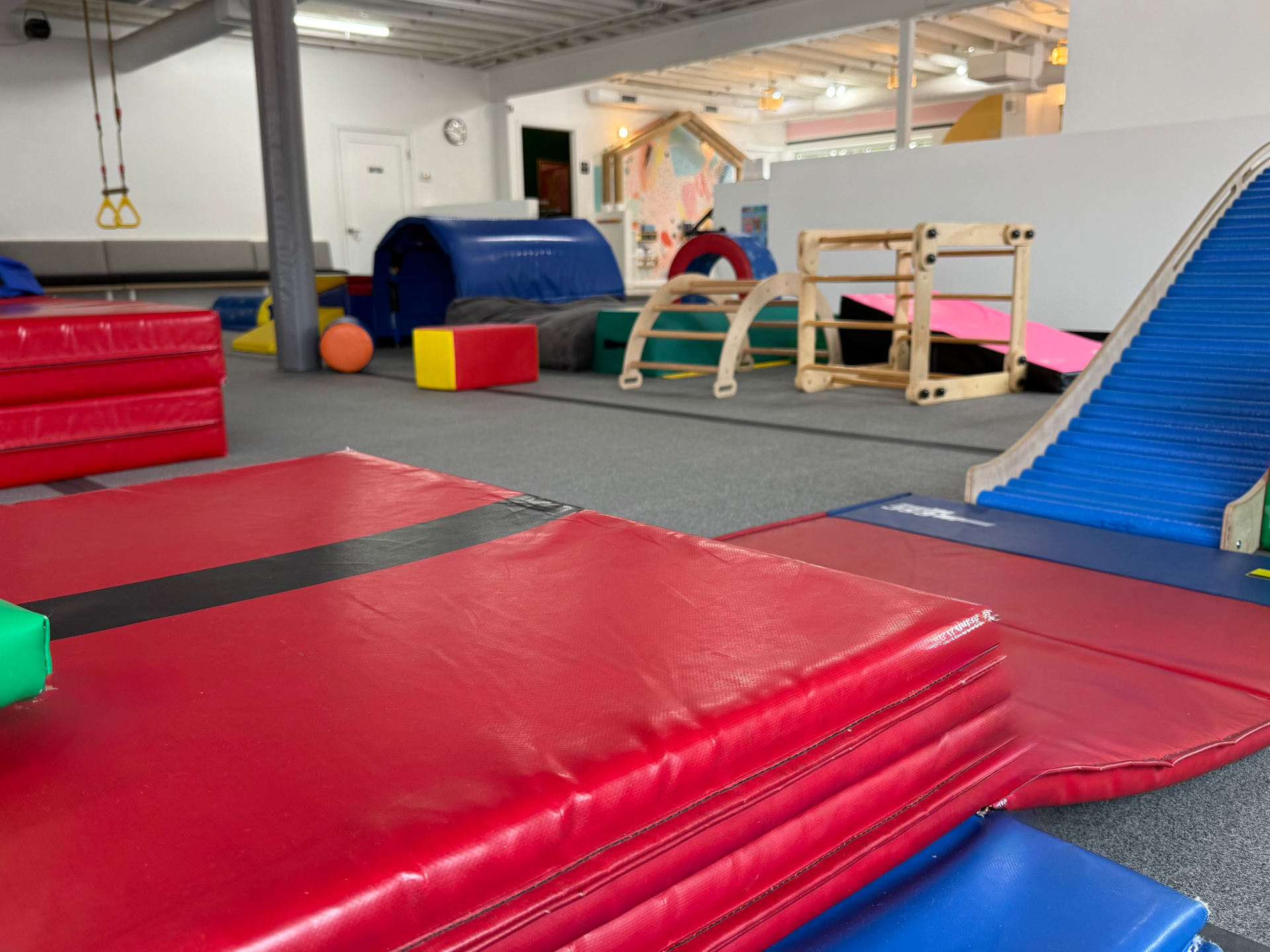 Red tumbling mats, wooden climbers, a blue slide and hanging rings in the open play space at tumble HAUS Denver