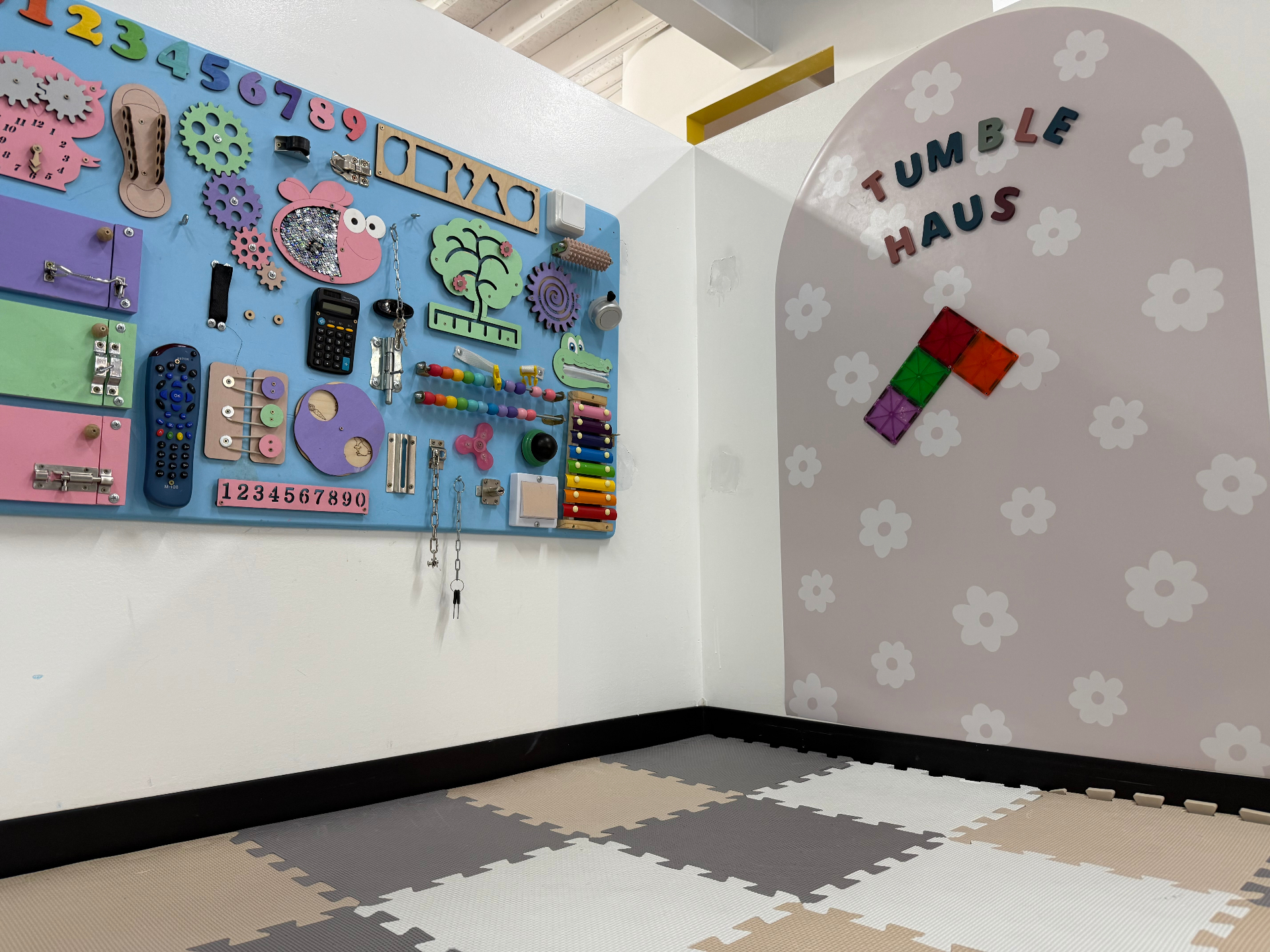 Sensory play corner at tumble HAUS with a busy board and branded flower mural wall