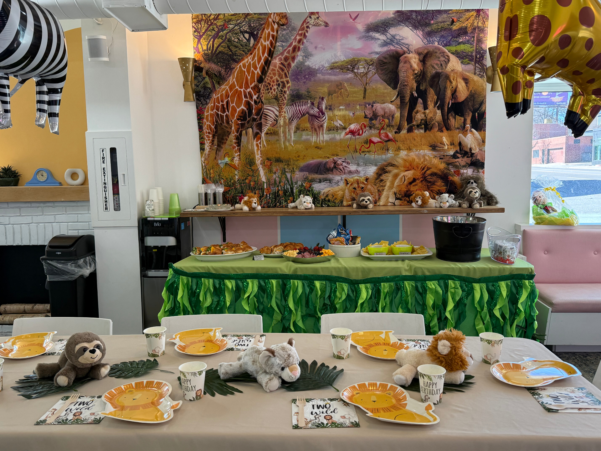 Safari themed birthday party at tumble HAUS with a jungle backdrop, plush animals, lion plates and a green grass food table
